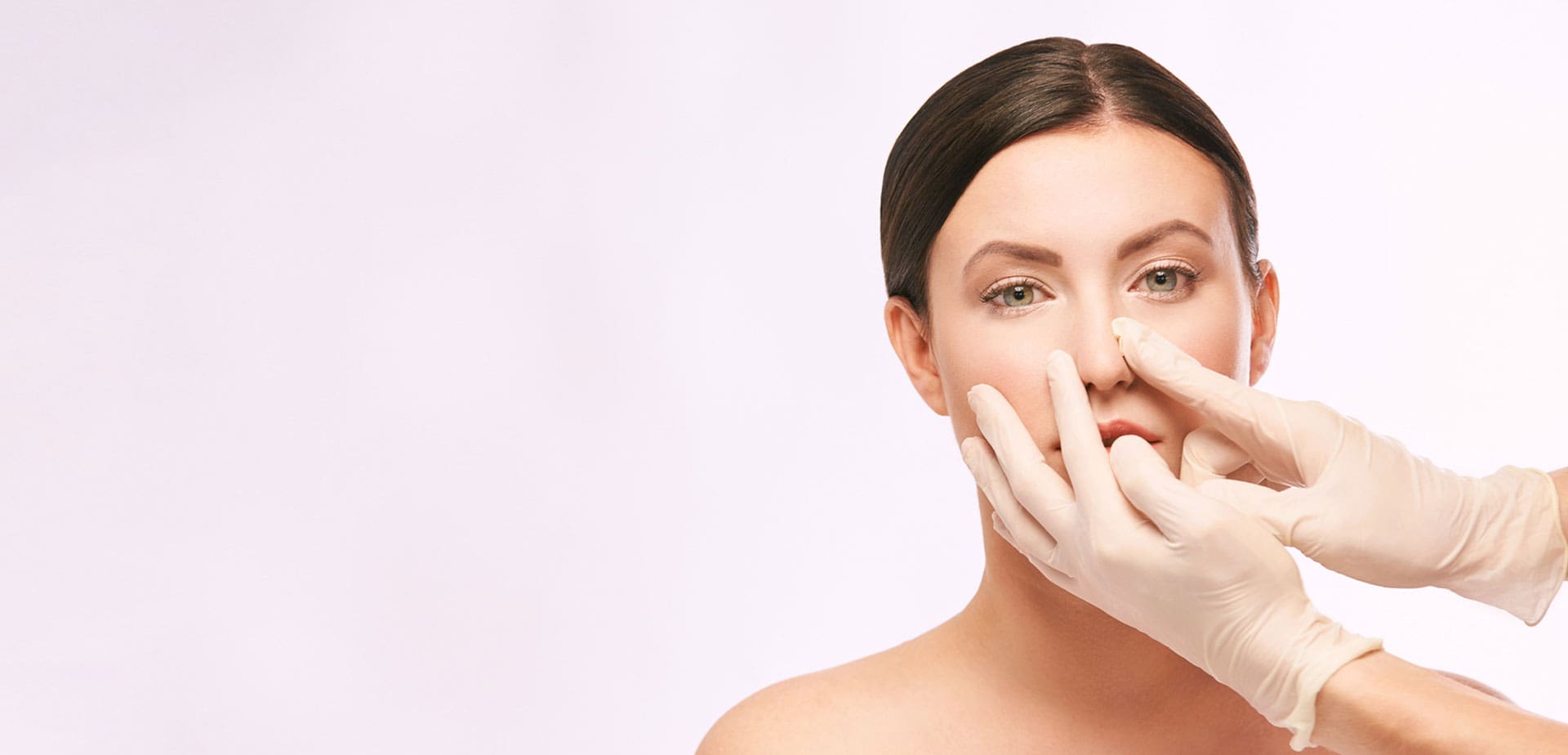 gloved-hand-examining-a-woman's-nose-against-a-pink-background