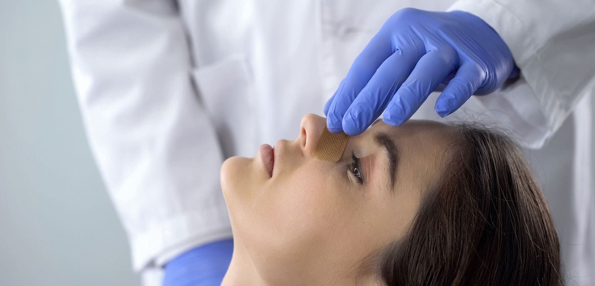 gloved-provider-examining-a-woman's-nose-while-she-lies-back