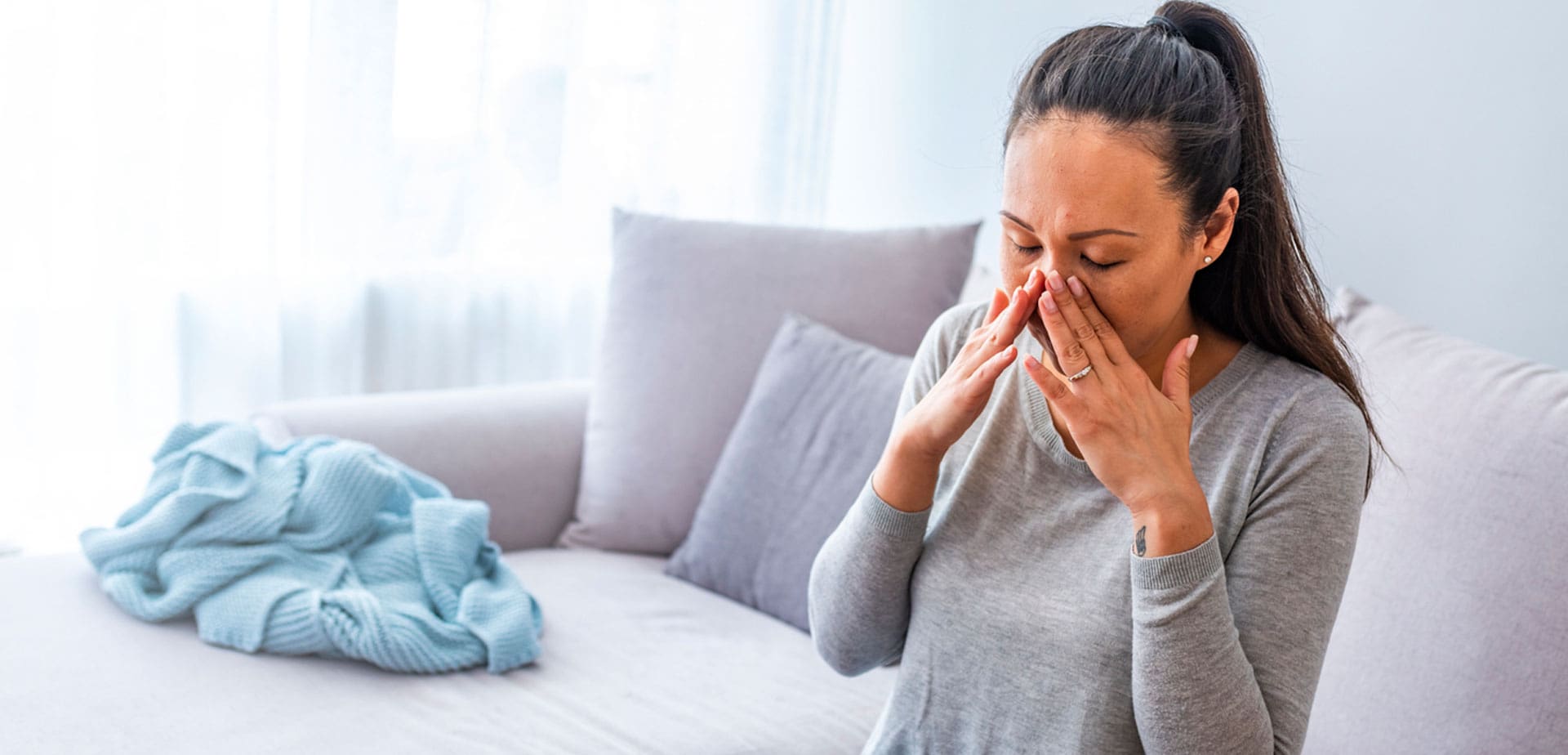 woman-sitting-on-a-couch-blowing-her-nose-into-a-tissue